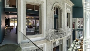 Interior de un hotel de varios niveles con arquitectura de piedra, un balcón con barandillas ornamentadas y vistas al exterior.