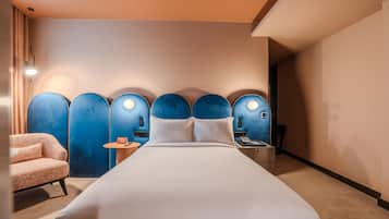 Een hotelkamer met een groot bed, een zithoek met een stoel, een bijzettafeltje en een aan de muur bevestigd toestel.