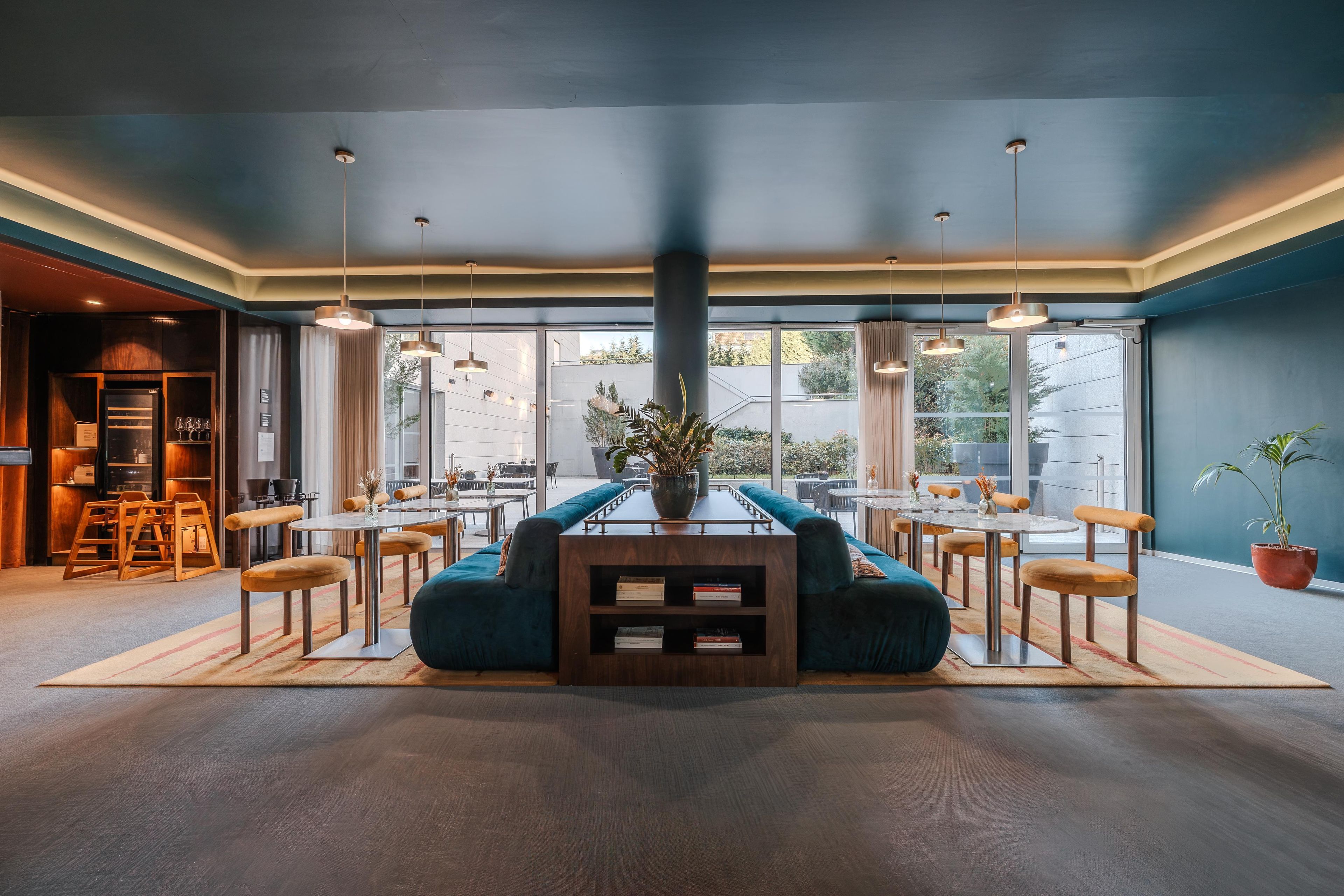 A modern dining area with a central seating arrangement, multiple tables, and a view of the outdoors.