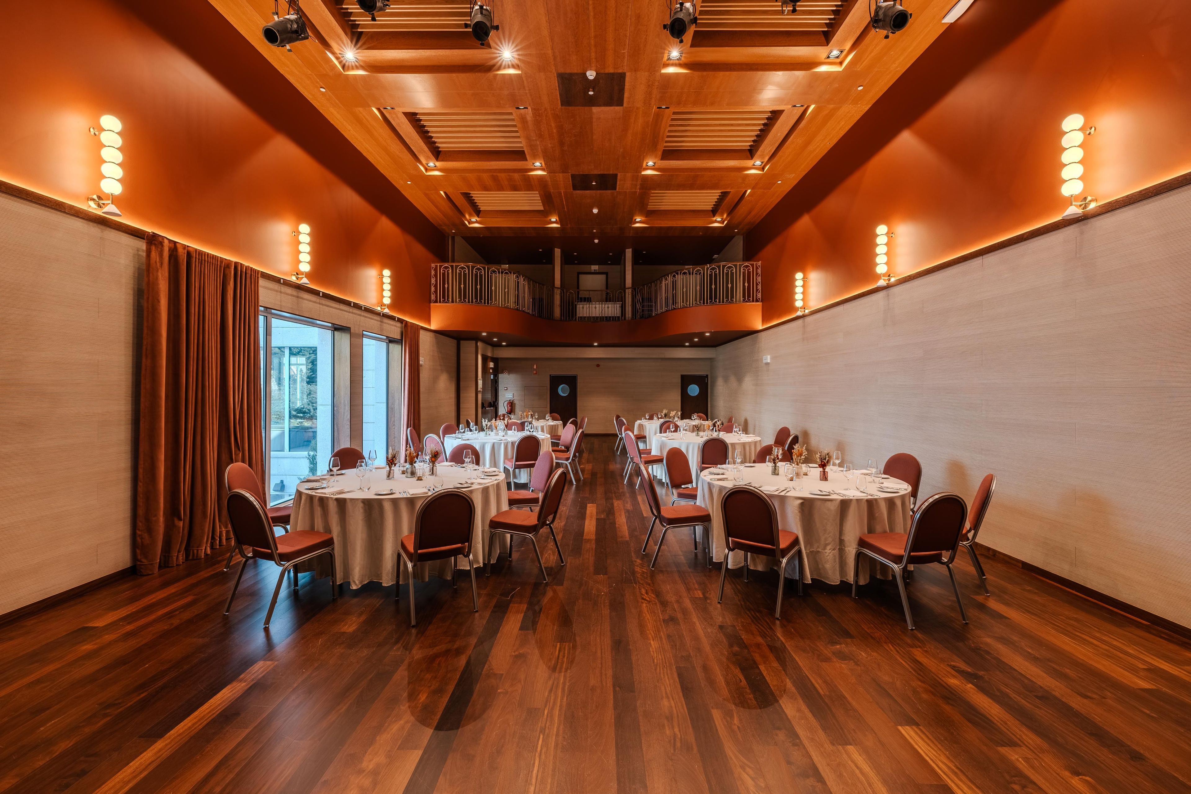 A conference room with round tables, chairs, and a wooden ceiling with recessed lighting.