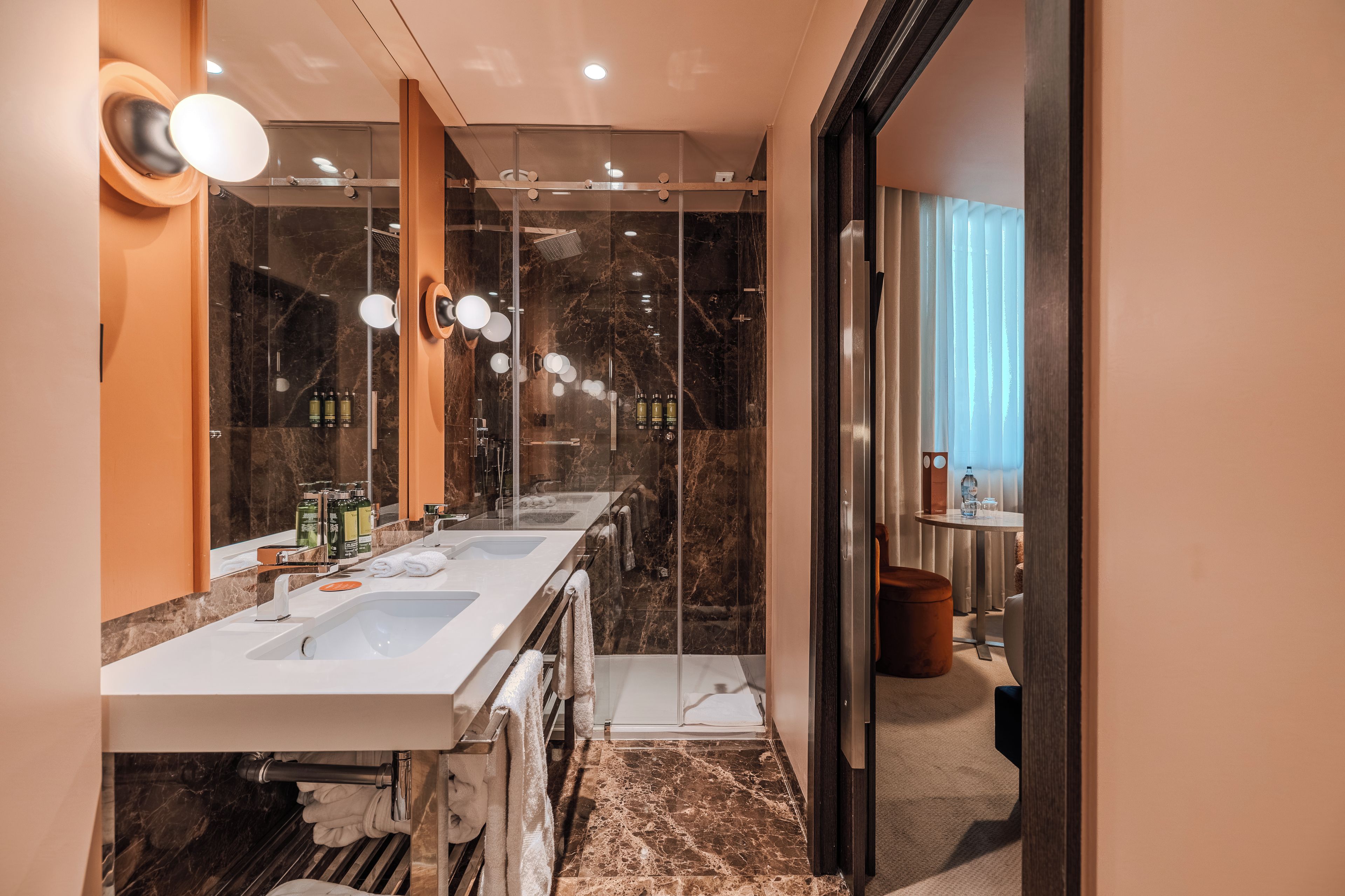 A modern bathroom with a glass-enclosed shower, a double sink vanity, and a marble-tiled floor.