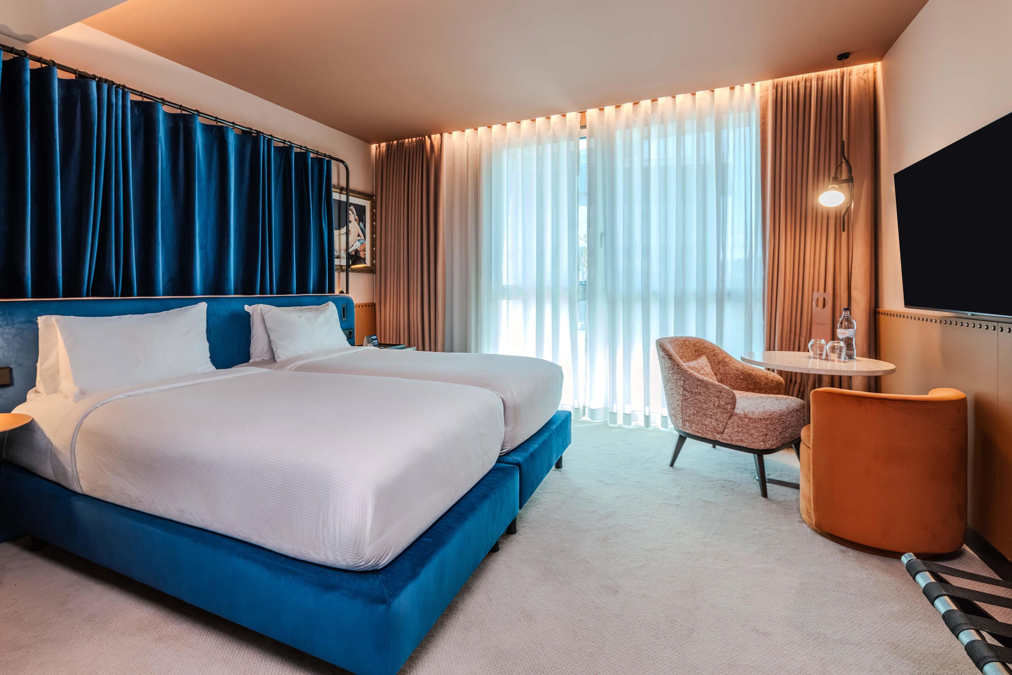 A hotel room with a large bed, a desk, a chair, and a TV.