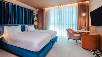 A hotel room with a large bed, a desk, a chair, and a TV.