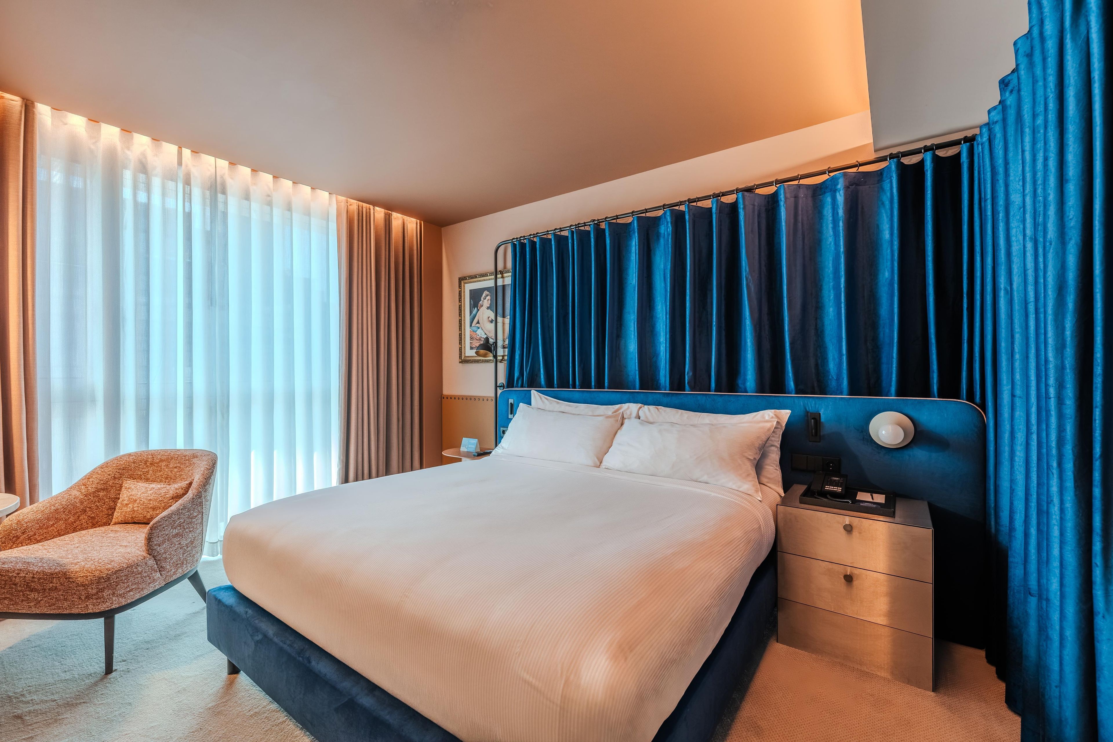 A hotel room with a large bed, a nightstand, a chair, and a window with curtains.