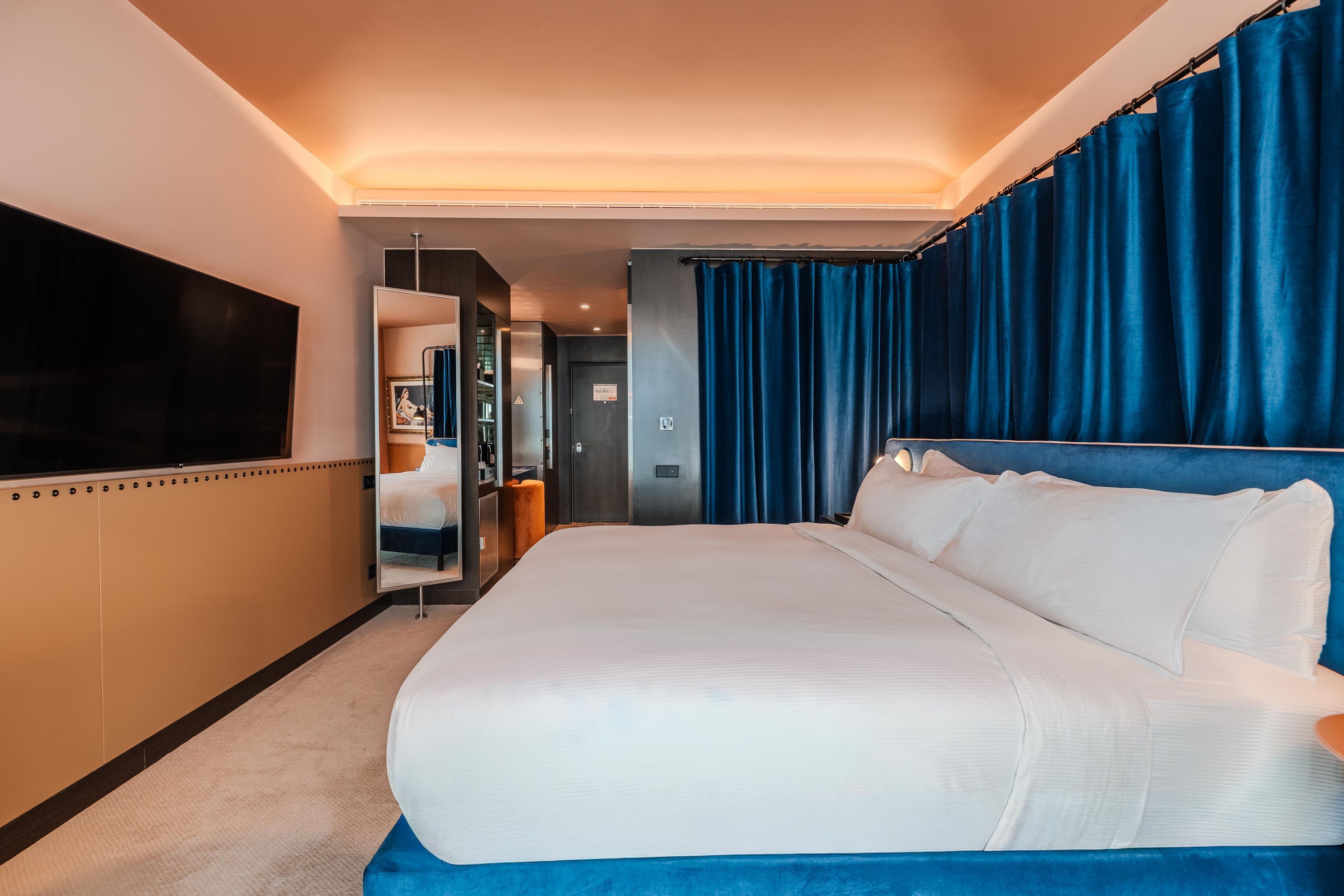 A hotel room with a large bed, a flat-screen TV, a bathroom with a mirror, and a door leading to another room.