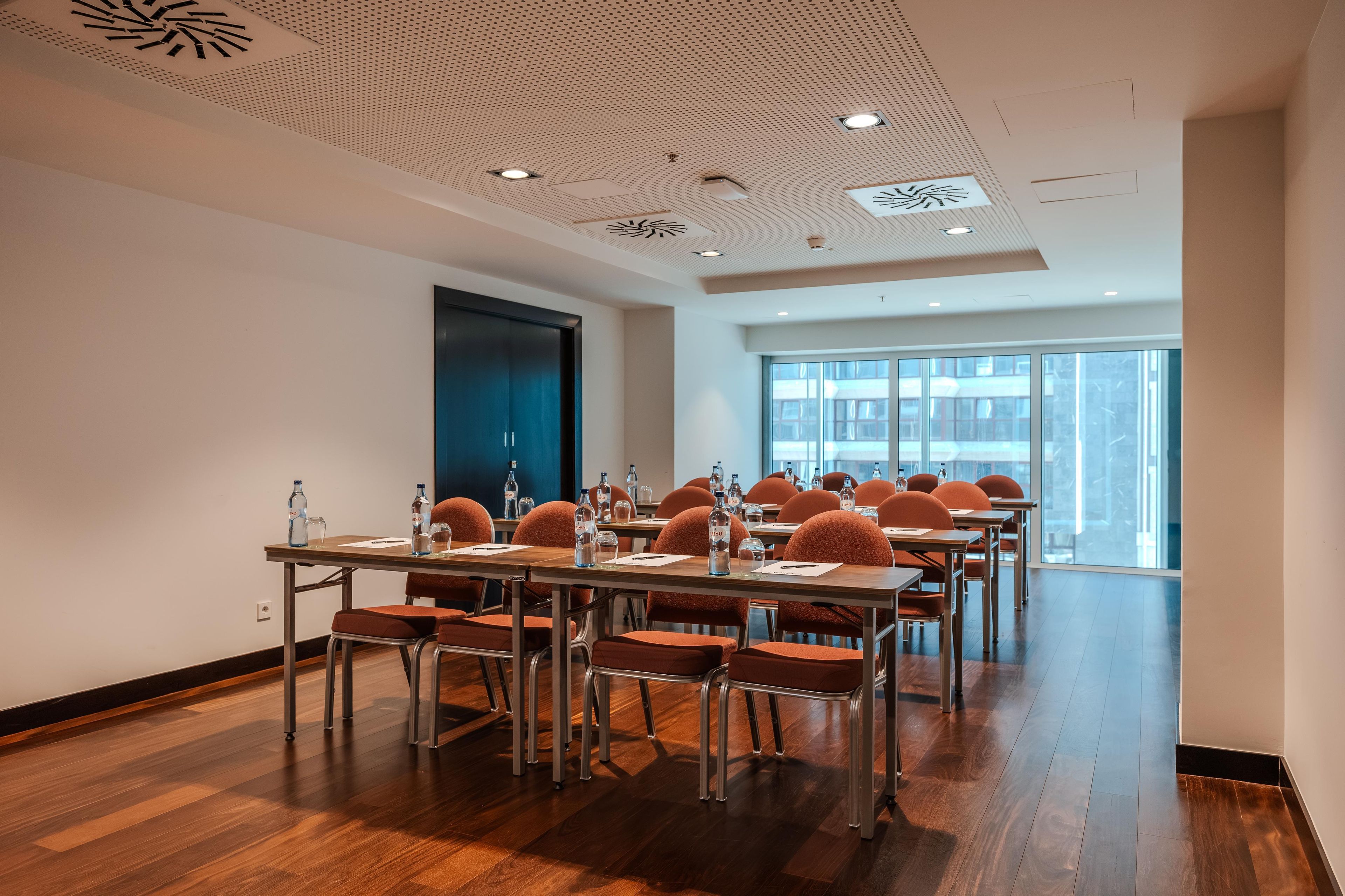 A conference room with a modern ceiling design, large windows, and a view of the cityscape.
