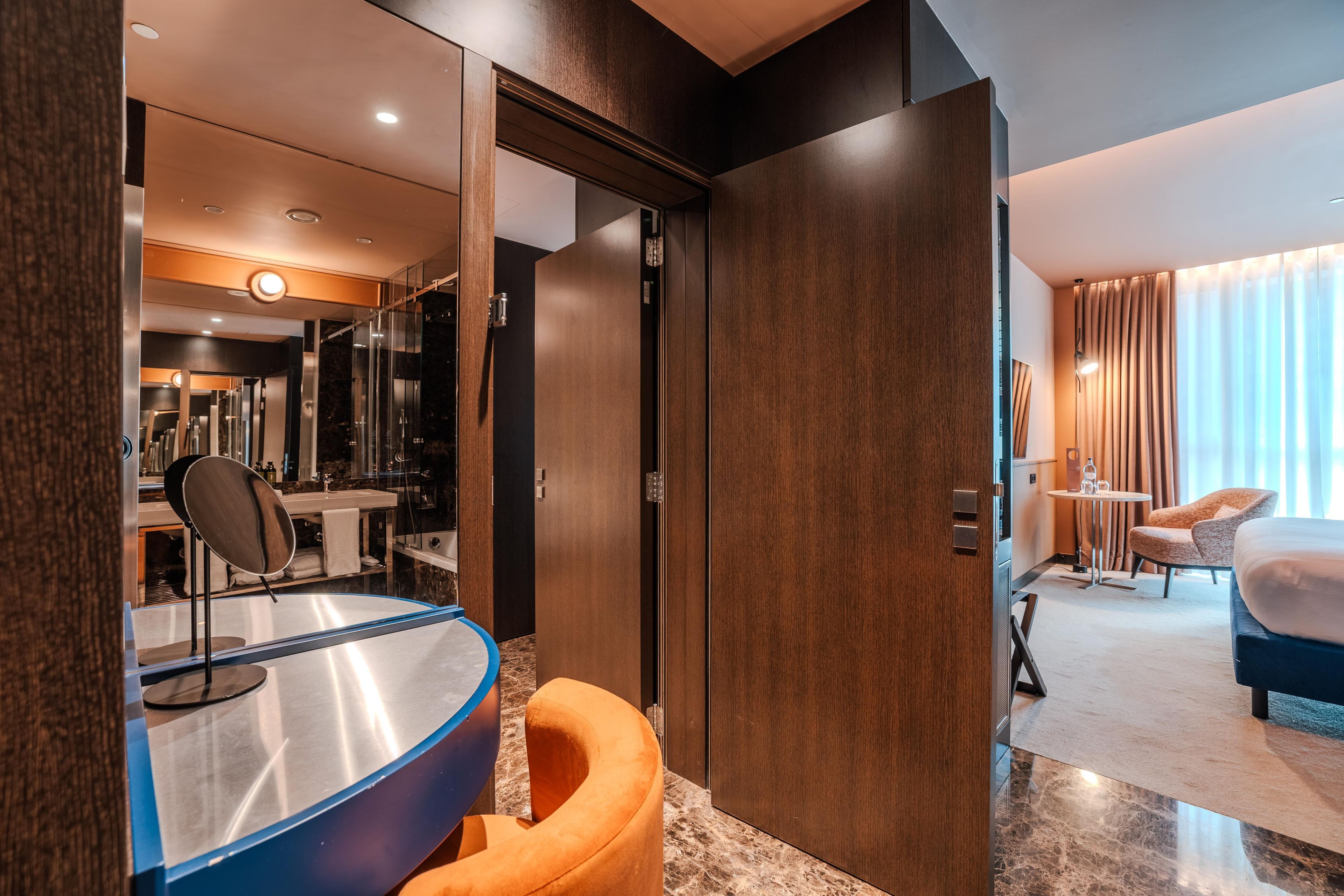 A hotel room with a bed, a desk, a chair, a bathroom, and a view of the outside.