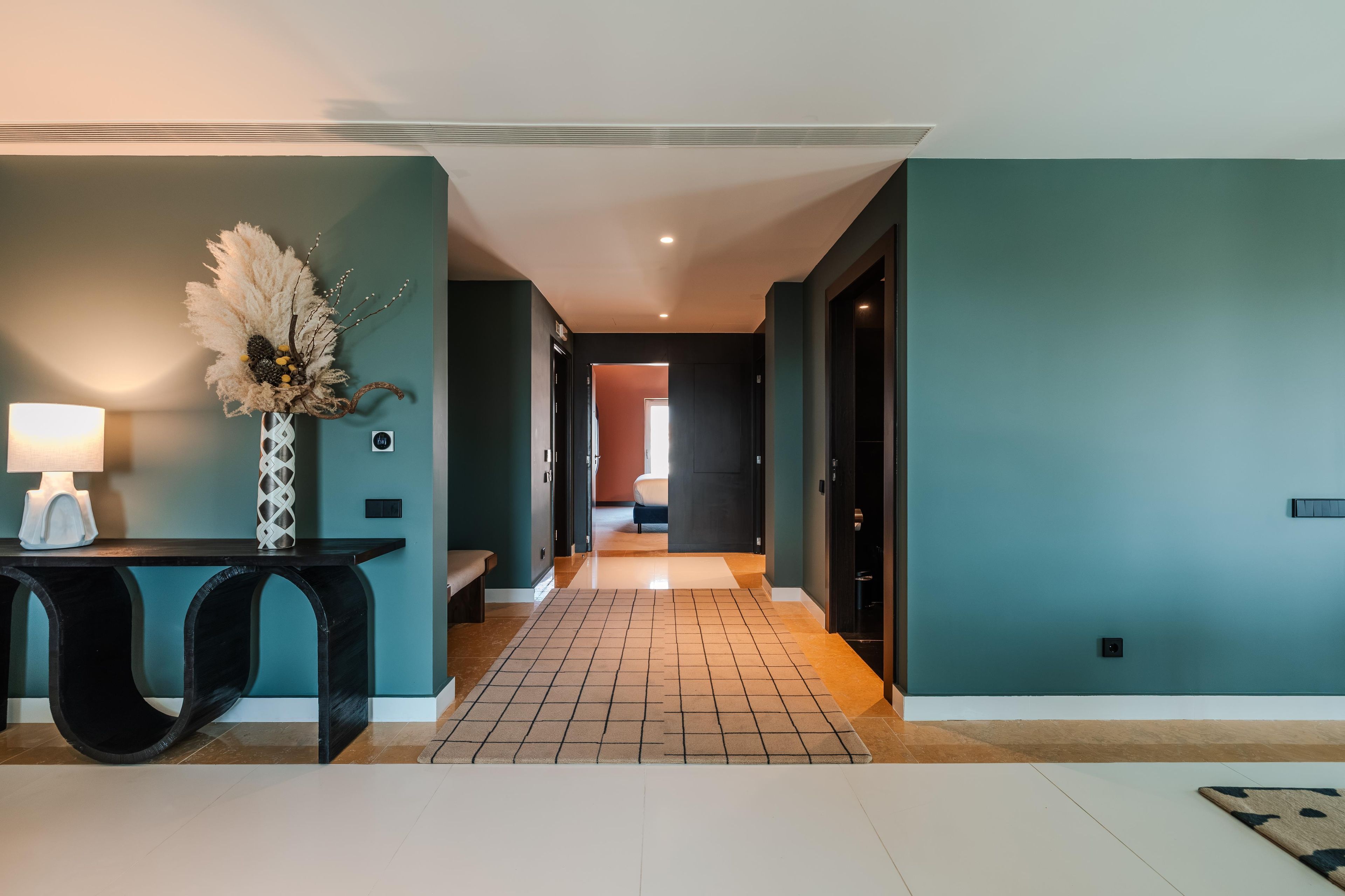 A hallway with a tiled floor, a desk with a lamp, and a decorative vase.
