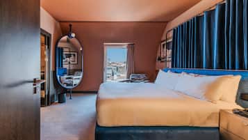Habitación de hotel con una cama grande, un espejo redondo, vistas de la ciudad y una ventana con cortinas.