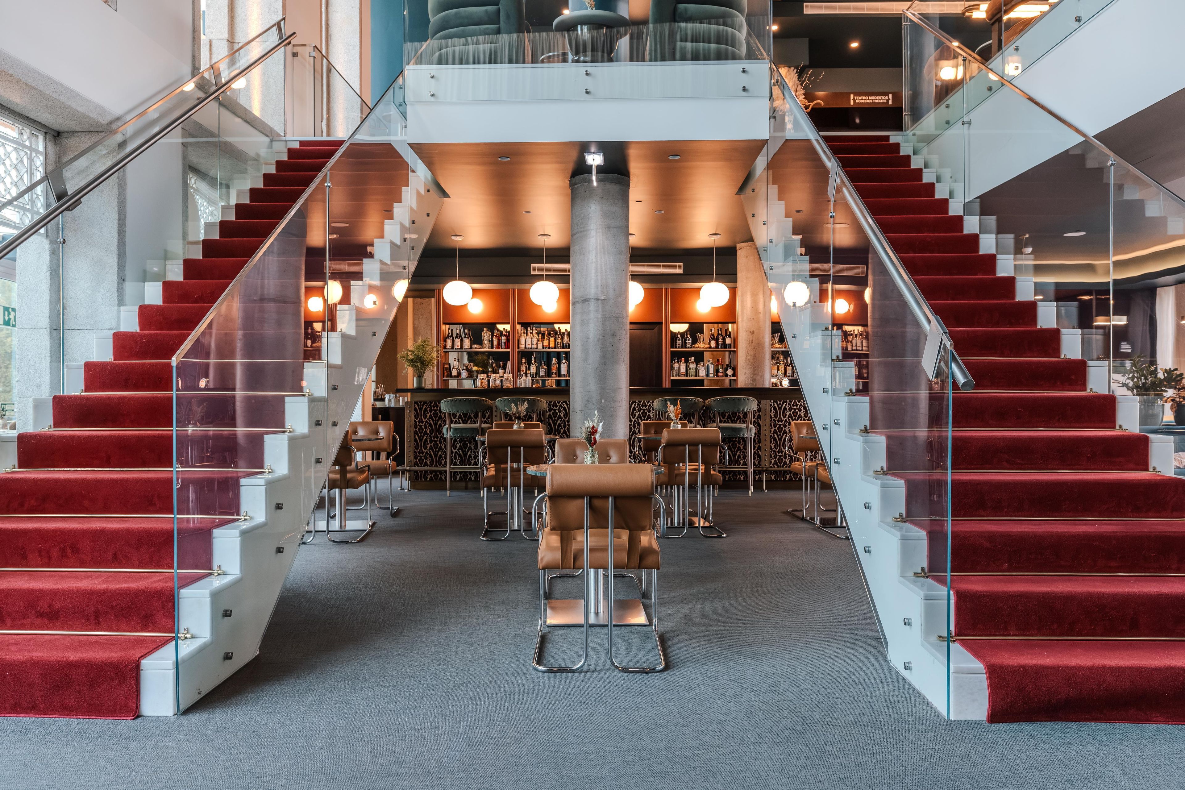 A hotel lobby with a grand staircase, seating area, and a bar.