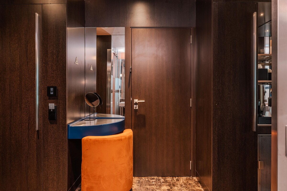 Un baño moderno con suelo de mármol, un lavabo azul y una silla naranja.