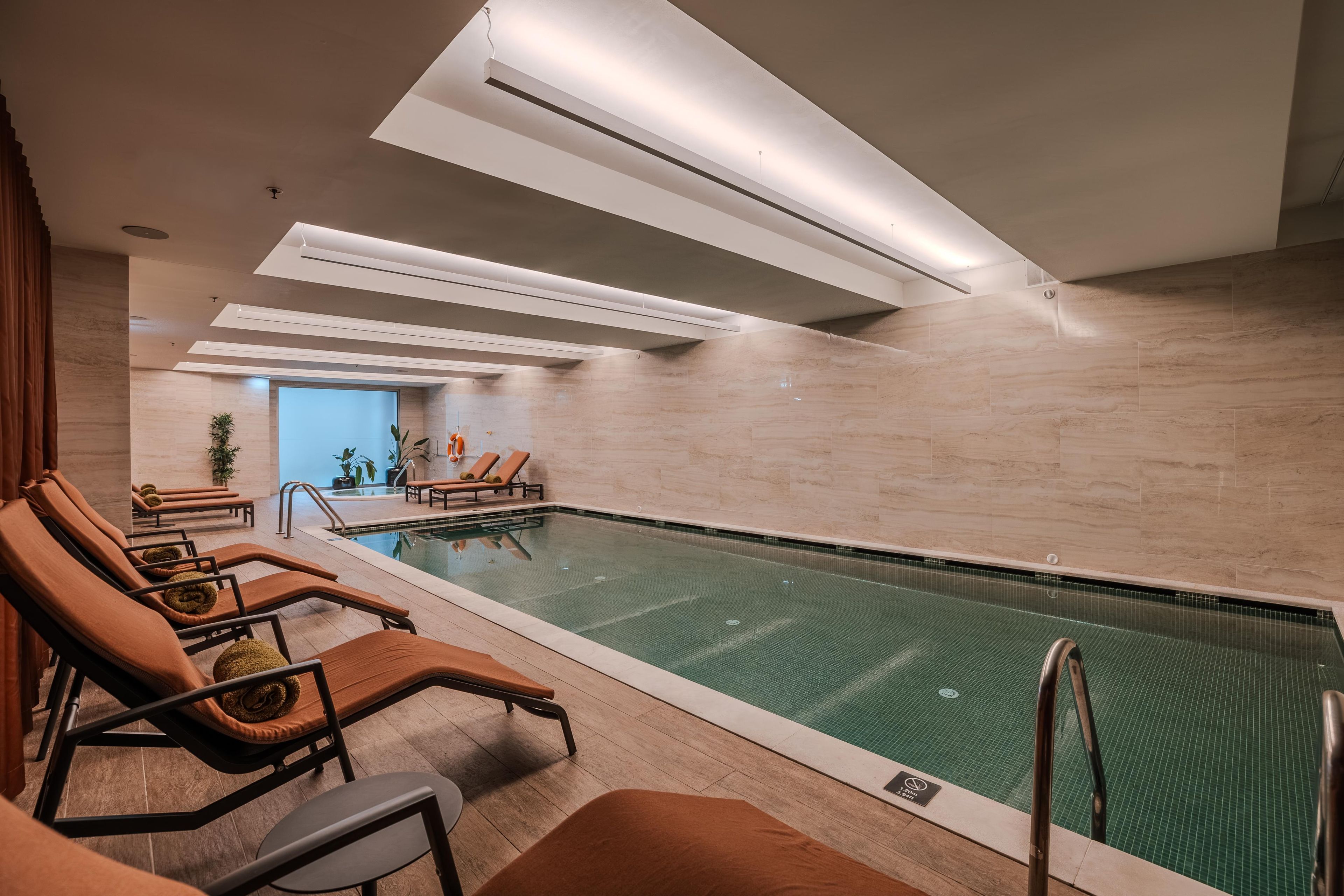An indoor swimming pool with lounge chairs and a clear view of the pool.