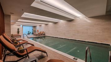 An indoor swimming pool with lounge chairs and a clear view of the pool.
