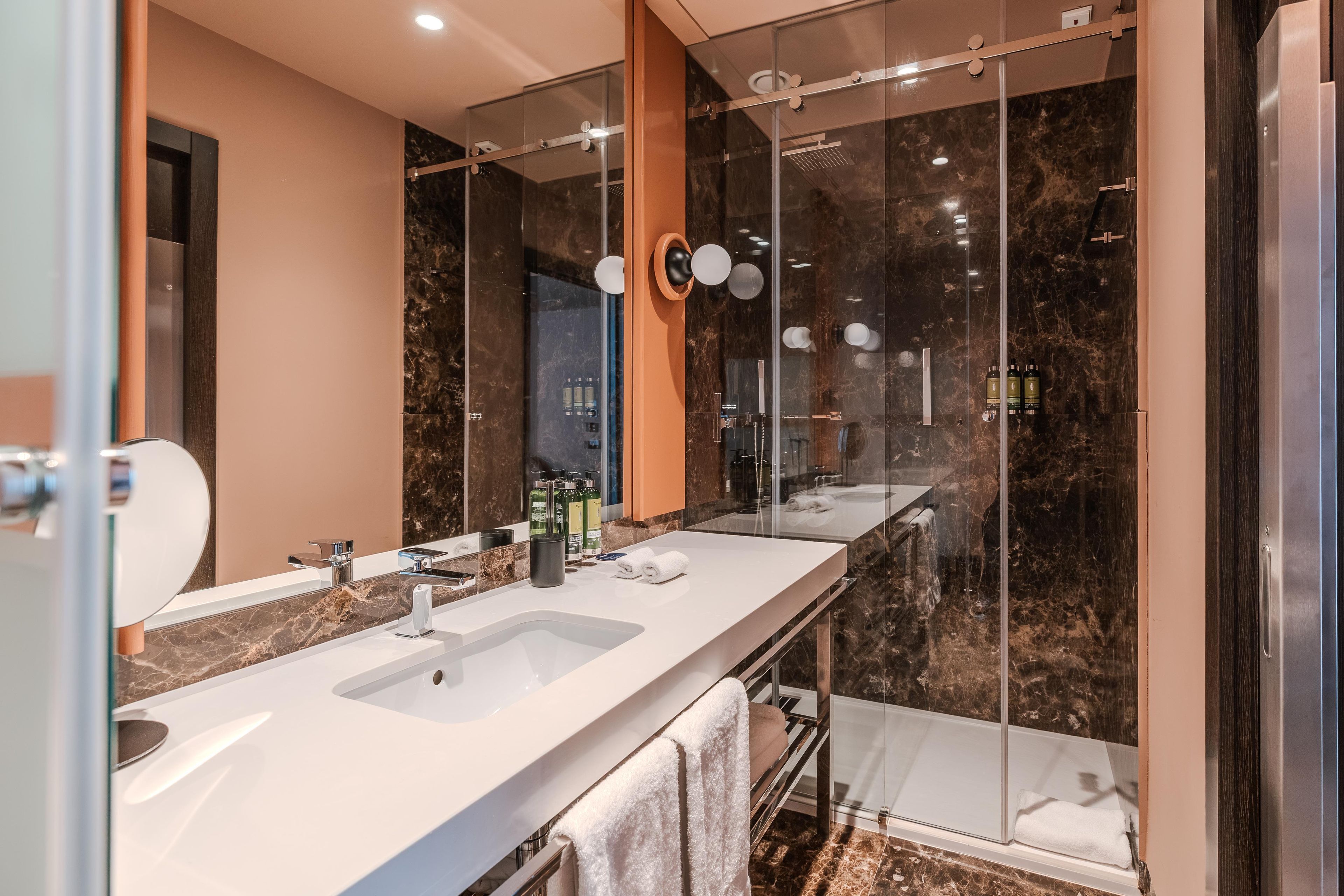 A modern bathroom with a double sink vanity, a glass shower enclosure, and a marble backsplash.