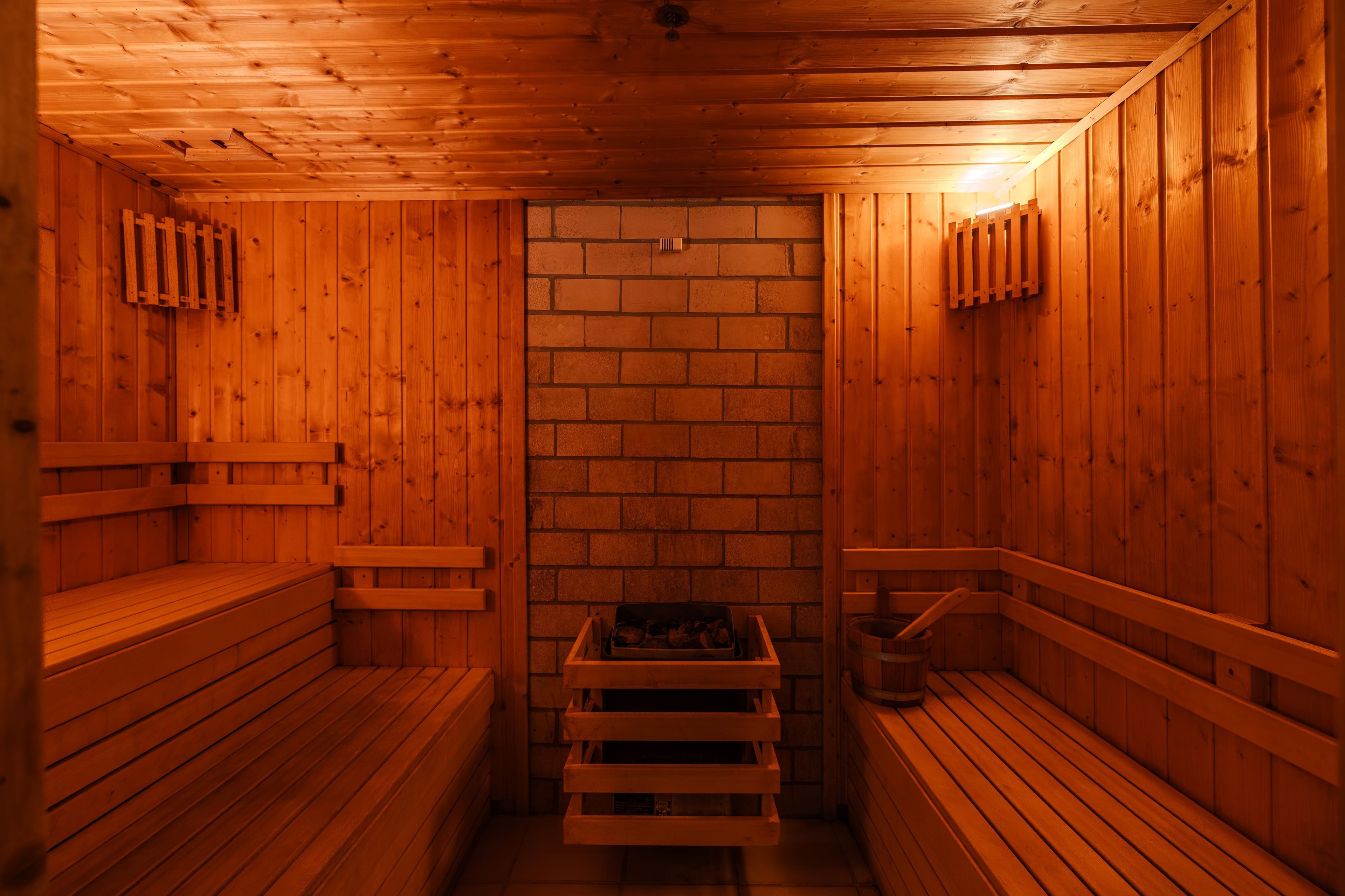Una sauna con paredes y bancos de madera, un muro de ladrillo en el centro y un banco con un cubo.