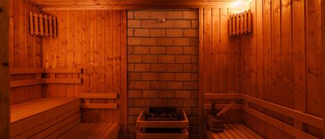 Una sauna con paredes y bancos de madera, un muro de ladrillo en el centro y un banco con un cubo.