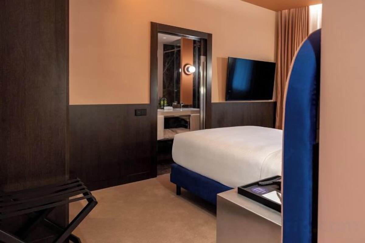 A hotel room with a bed, a TV, a mirror, and a desk.