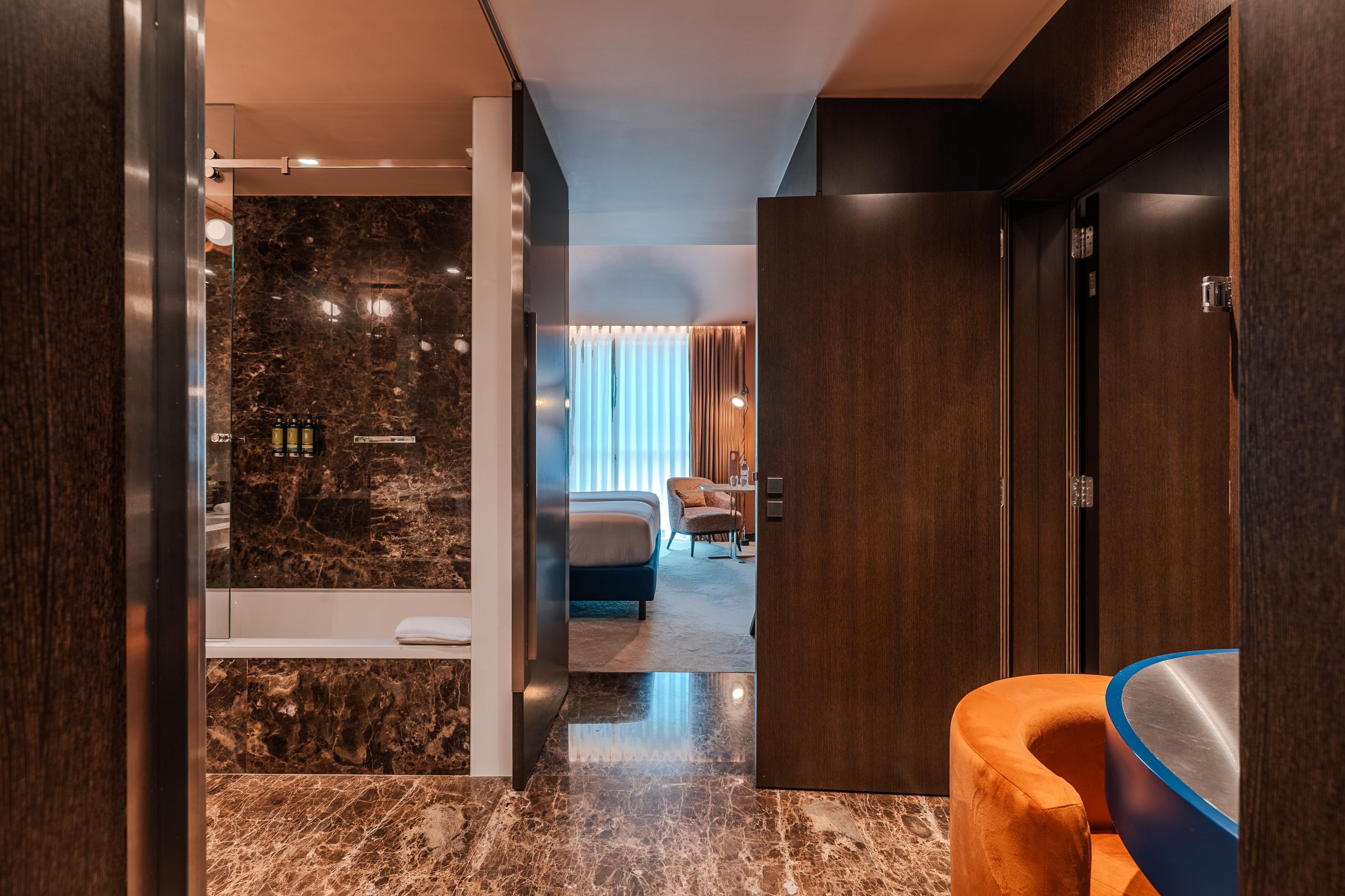 Une chambre d’hôtel avec un sol en marbre, un lit, un coin salon et une salle de bain avec douche.