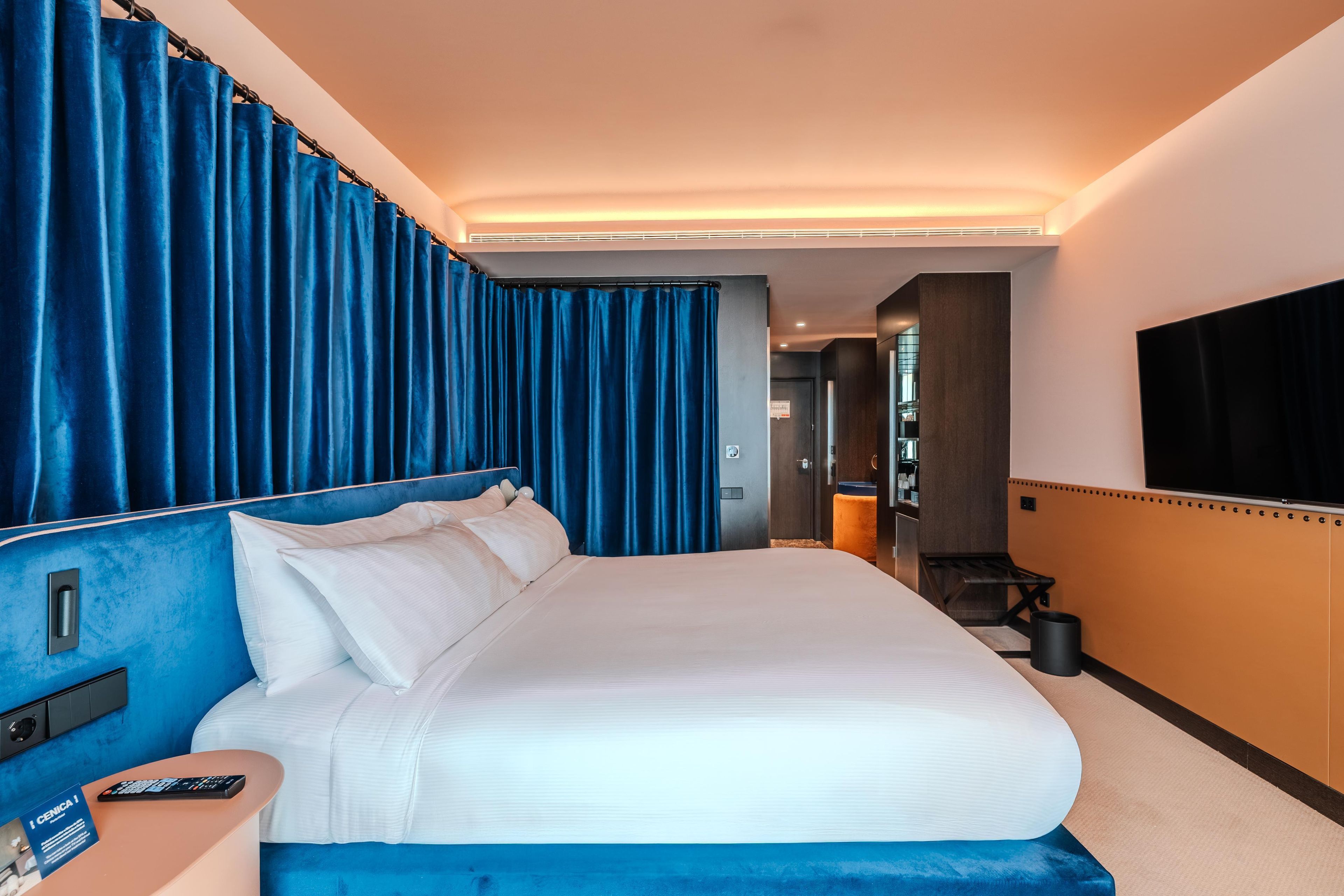 Habitación de hotel con una cama grande, un televisor montado en la pared y un baño visible a través de una puerta abierta.