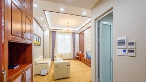 Habitación de hotel con alfombra color crema, un sofá, una mesita, un televisor y una puerta con panel de vidrio.