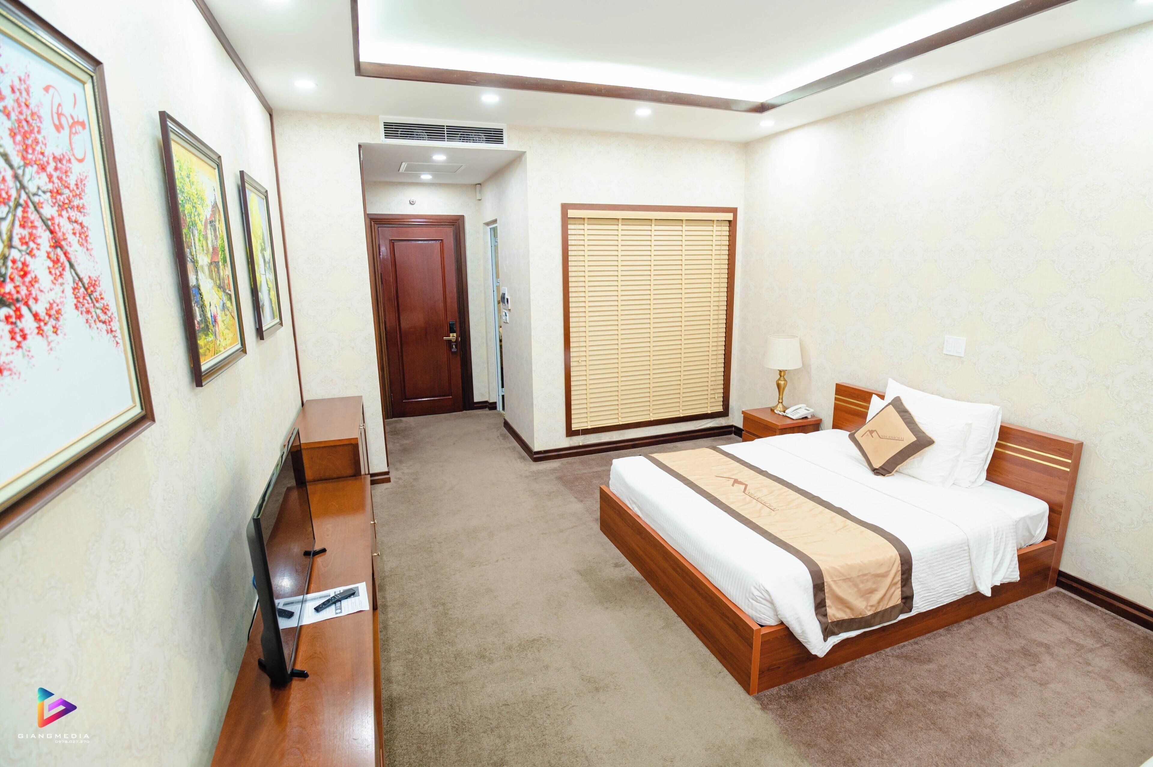 Quarto de hotel com cama, mesa de cabeceira, abajur e quadro na parede.