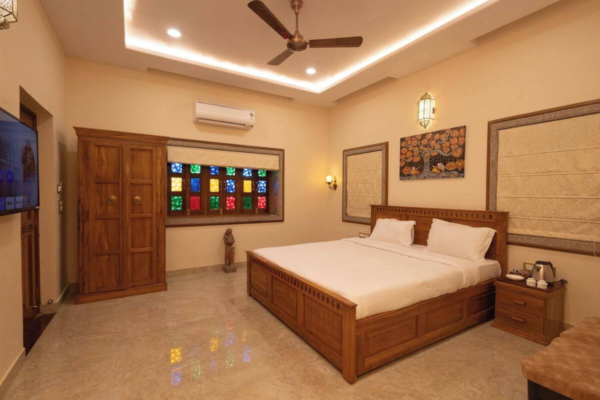 A bedroom with a wooden bed, a nightstand, a TV, a ceiling fan, and a stained glass window.