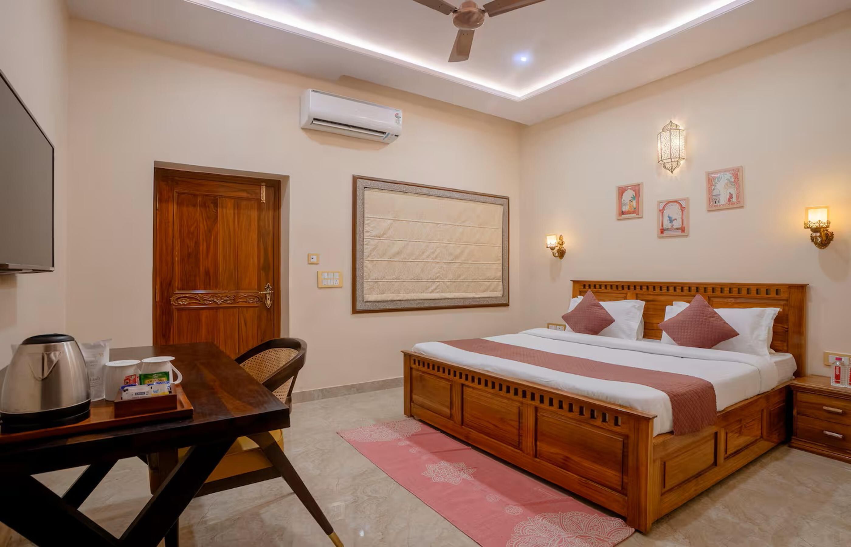 Quarto com cama de madeira, escrivaninha com chaleira, cadeira e mesa de cabeceira com abajur.