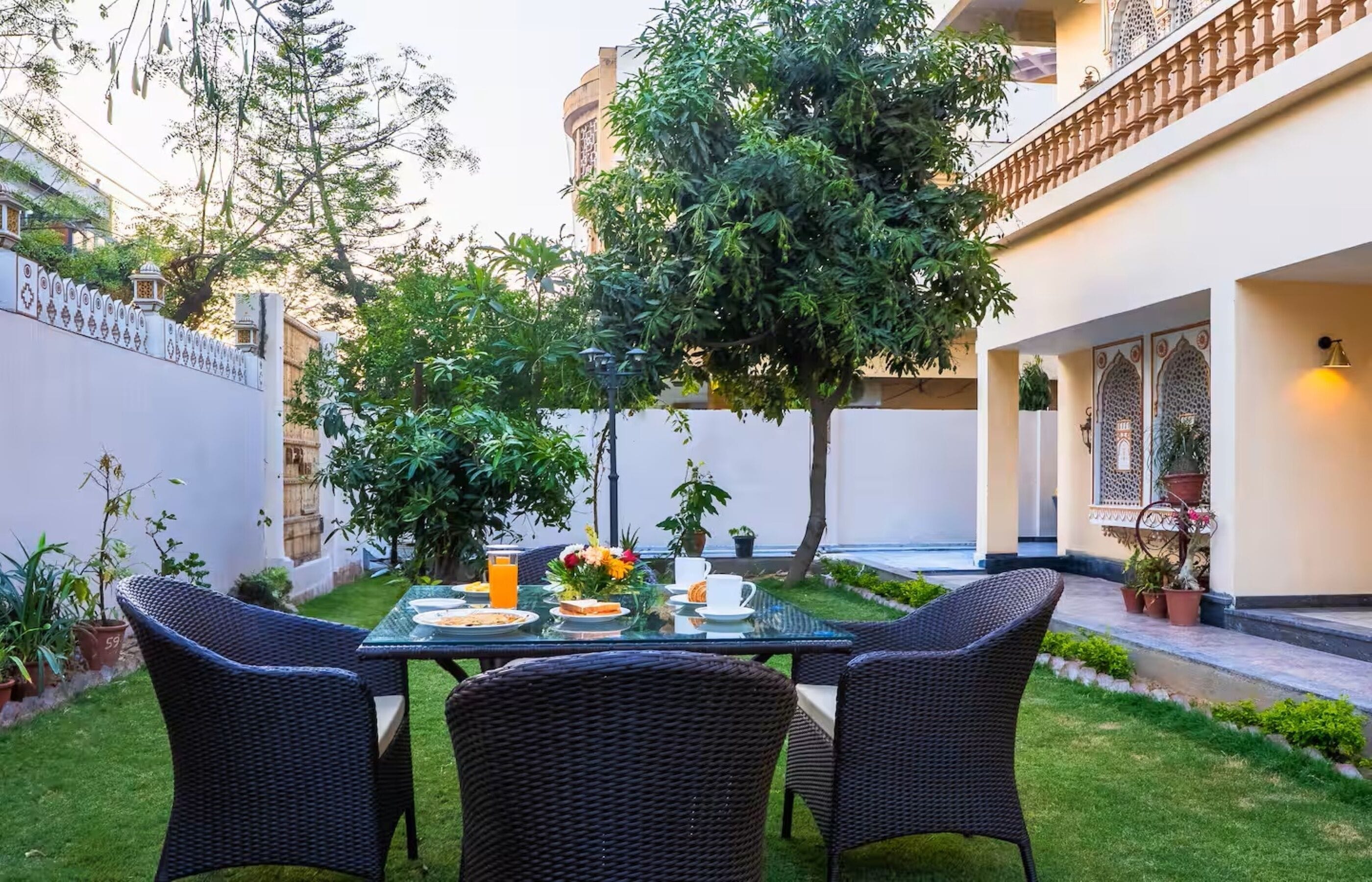 A dining area with a table set for two, surrounded by greenery and potted plants.