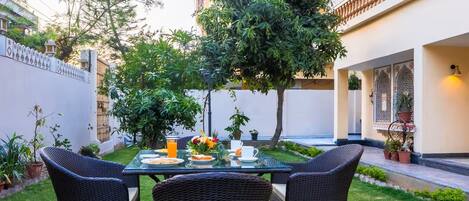 A dining area with a table set for two, surrounded by greenery and potted plants.