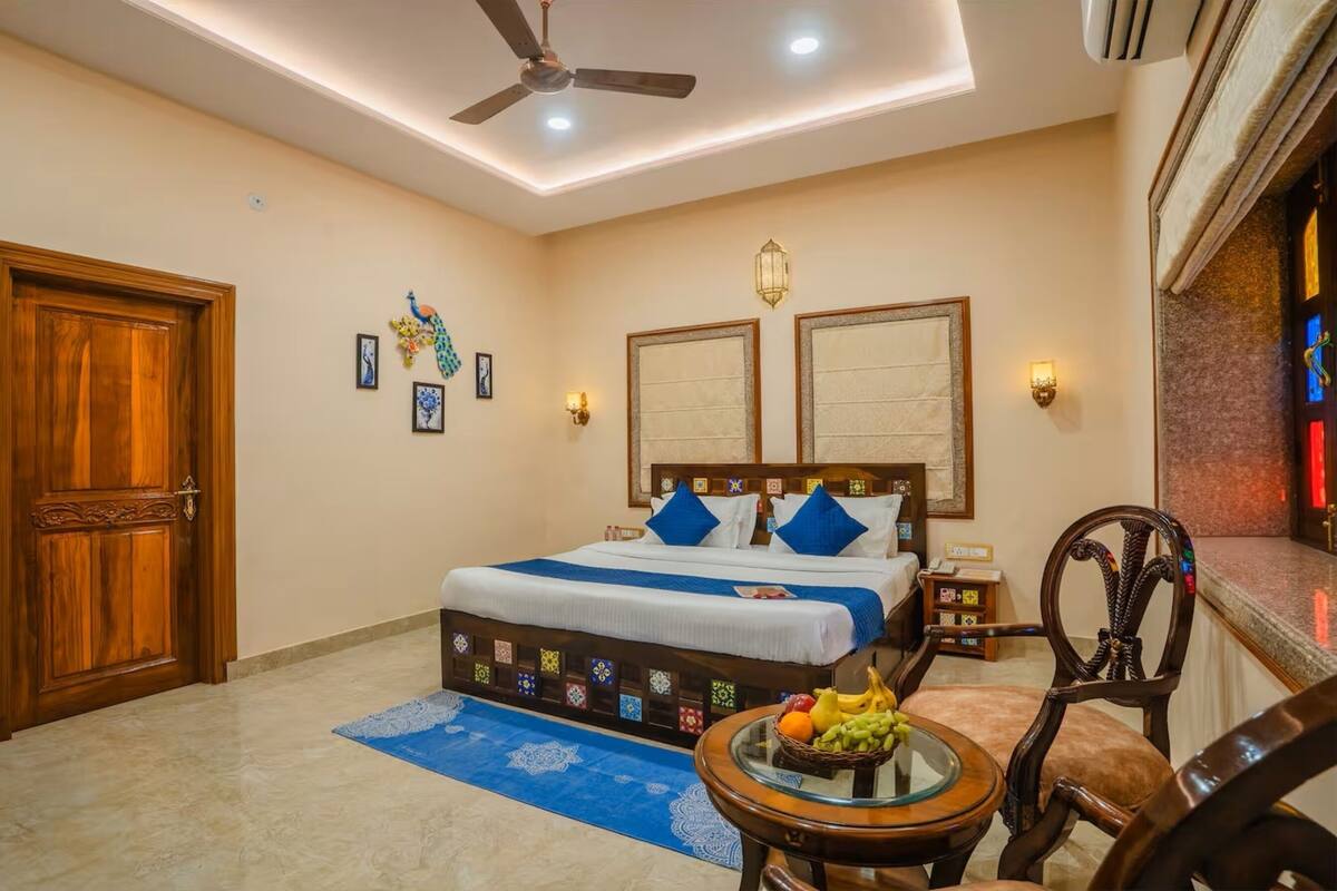 A bedroom with a bed, a ceiling fan, a nightstand, a chair, and a small table with fruit.
