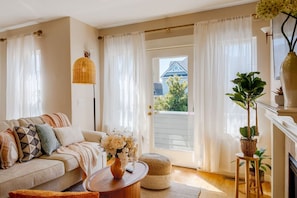 A living room with a sofa, a coffee table with a vase, a floor lamp, and a view through a door.