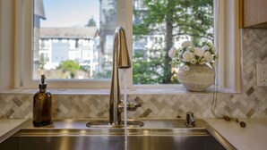 A kitchen with a stainless steel sink, a faucet, and a window with a view of buildings and trees. - Spacious 3B/2.5B Home in the Heart of Capitol Hill (Seattle)