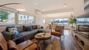 A modern living room with a sofa, armchairs, a coffee table, and a dining area with a view of a lake.