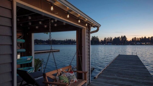 A wooden deck with a swing chair and a view of a lake at dusk.