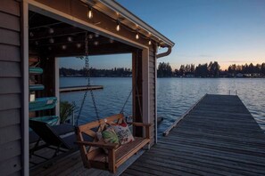 A wooden deck with a swing chair and a view of a lake at dusk. - Stunning 3b1bHome w/ Lake Access (Spanaway)