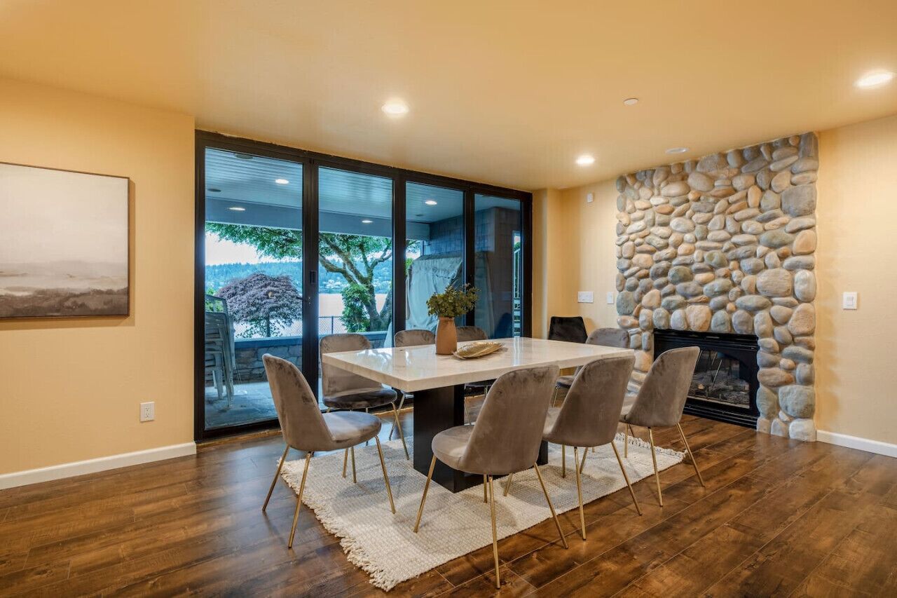 A dining area with a large table, six chairs, and a stone fireplace.