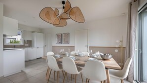 A modern kitchen with white cabinets, a dining area with a wooden table set for four, and a large window with curtains. - 650m from the sea, modern house for 7 (Piriac-sur-Mer)