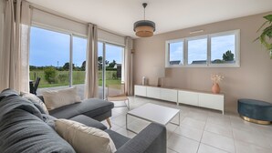 A modern living room with a grey sofa, a white coffee table, and a view of a garden through large windows. - 650m from the sea, modern house for 7 (Piriac-sur-Mer)