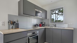 Una cocina moderna con armarios grises, horno empotrado, cafetera y ventana con vistas a árboles.