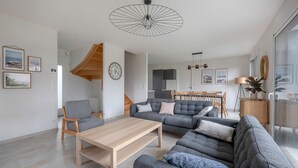 Una sala de estar moderna con un sofá gris, una mesa de centro de madera y un comedor con una mesa y sillas de madera.