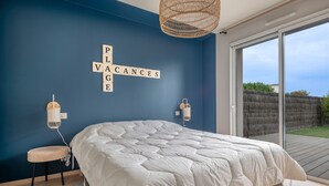 Un dormitorio con una cama grande, una lámpara de pared y vistas al exterior a través de un ventanal corredero.