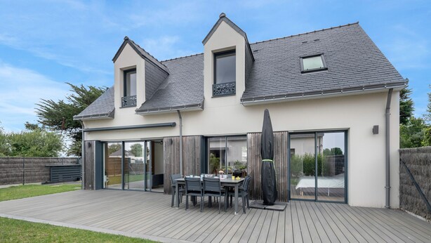Una casa moderna con terraza, puertas correderas de vidrio y un área de comedor con mobiliario exterior.