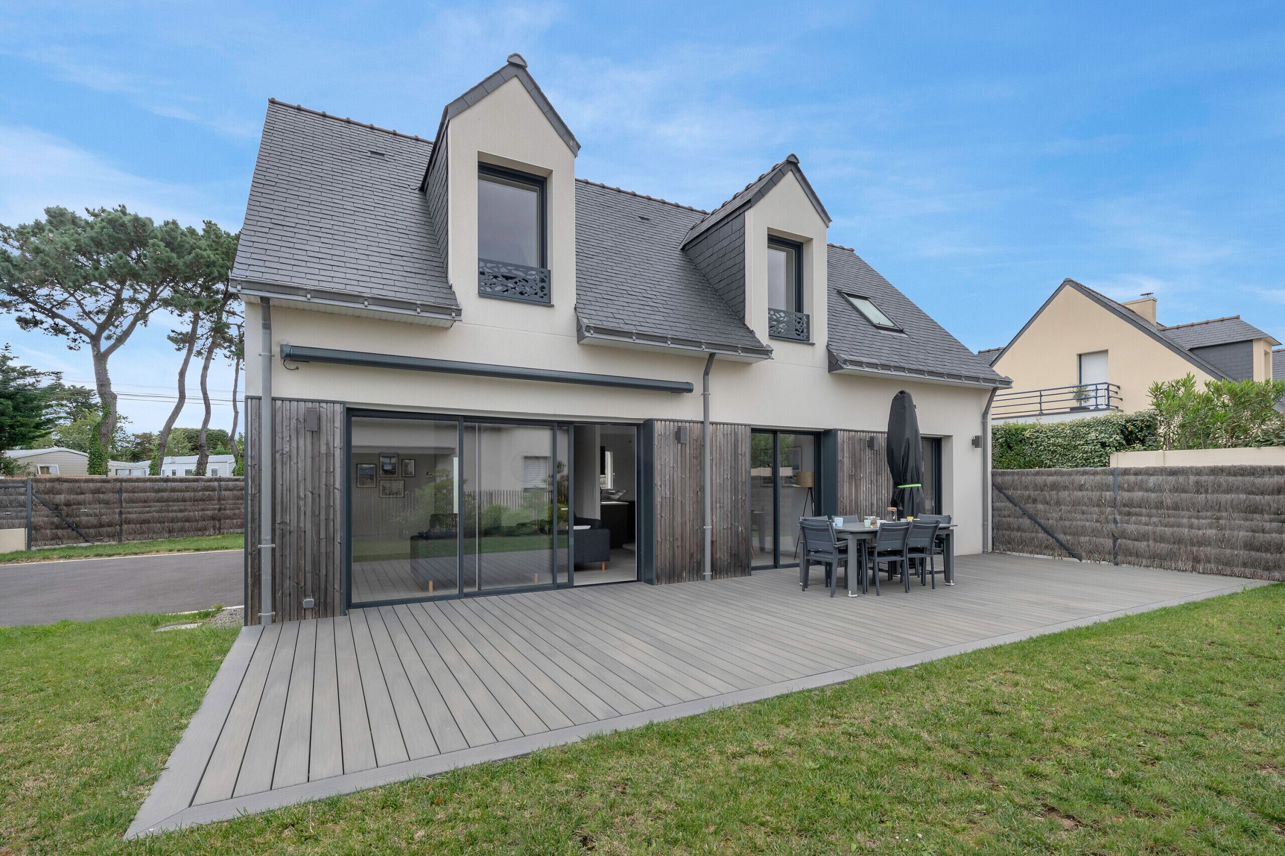 Une maison moderne dotée d’une grande terrasse, de portes-fenêtres coulissantes et d’un coin repas.
