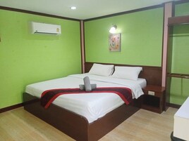 A hotel room with a bed, an air conditioner, a nightstand, and a wall-mounted light fixture.