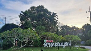 A sign with a house symbol and text, surrounded by greenery and trees. - Haad Somboon House (Bang Saphan)