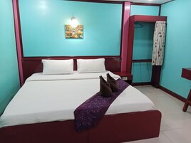 A neatly made bed with white linens and a purple throw blanket, a wall-mounted light fixture, and a painting of a cityscape.