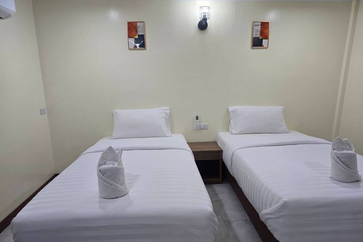 Habitación de hotel con dos camas individuales, cada una con una almohada blanca y una toalla. Hay dos mesitas de noche, una lámpara de pared y un cuadro pequeño en la pared.