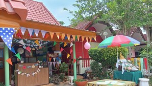 A colorful outdoor area with a wooden structure, potted plants, and a Buddha statue. - Haad Somboon House (Bang Saphan)