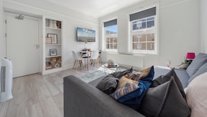 A modern living room with a grey sofa, a dining area with a table and chairs, and large windows with a city view. - King's Cross Boutique Apartment! ZONE 1 !!! (London)