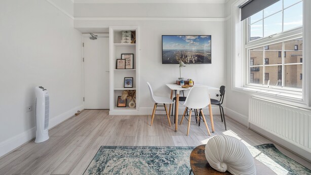 A modern, well-lit room with a dining area, a built-in shelf with decorative items, and a large window offering a city view. - King's Cross Boutique Apartment! ZONE 1 !!! (London)